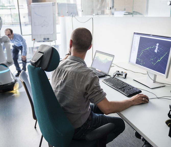 Kaksi henkilöä työskentelee robotin kanssa