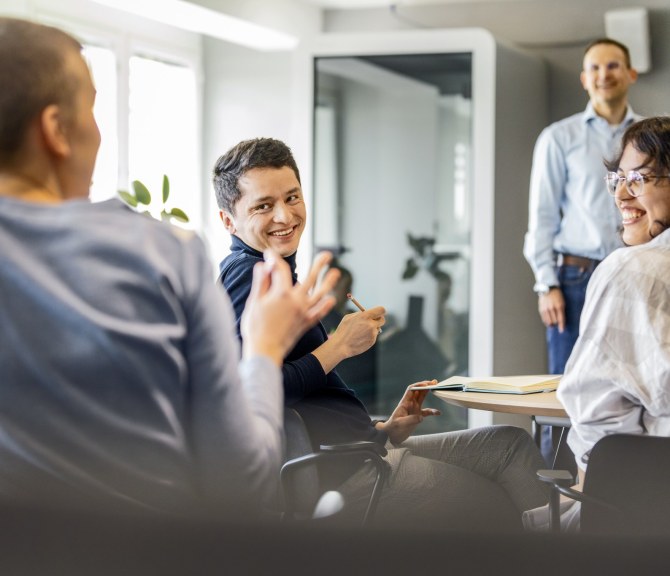 Henkilöitä tapahtumassa, puhuja edessä ja yleisö juttelee toisilleen.