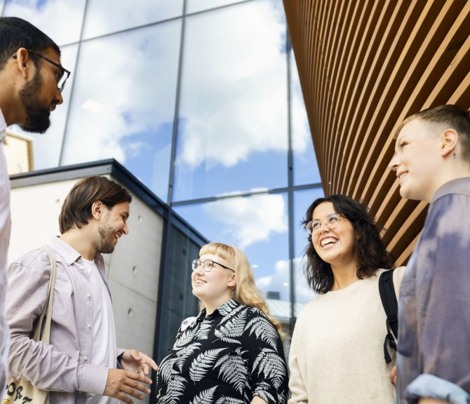 Henkilöitä seisoo ulkona rakennuksen edessä.