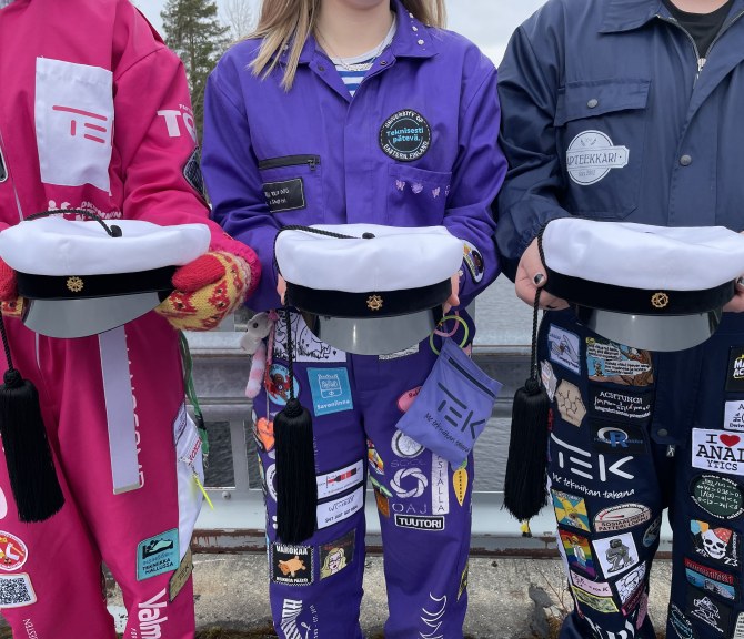 Kolme opiskelijahaalareihin pukeutunutta henkilöä pitelee uutta, itäsuomalaista tupsulakkia.