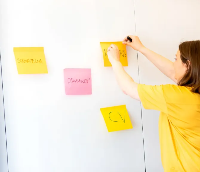Uravalmentaja laittaa post-it lappuja valkotaululle