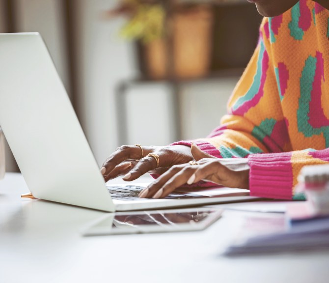 Värikkääseen neuleeseen pukeutunut nuorehko henkilö läppärin ääressä.