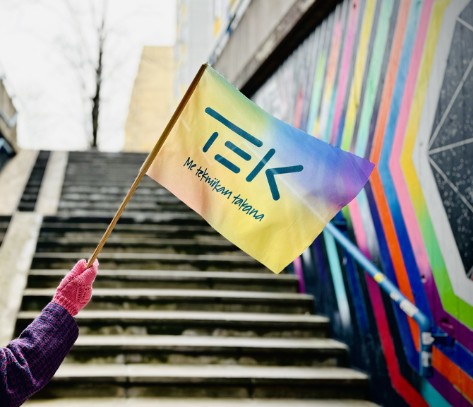 Henkilö heiluttaa TEKin sateenkaarevaa lippua värikkään portaikon alla.