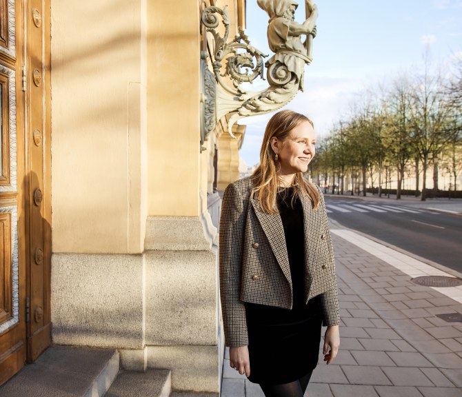 Heta Kosonen seisoo kadulla, ulko-oven edessä.