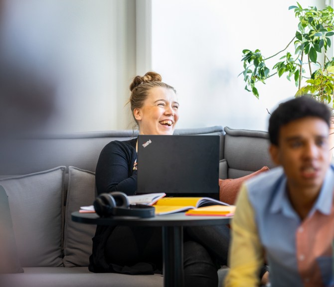 Kaksi henkilöä lounge-tilassa, taaimmainen iloitsee.
