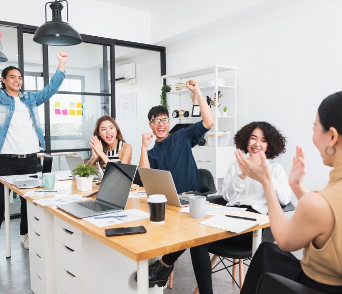 Ihmisiä, kädet ylhäällä, pöytä