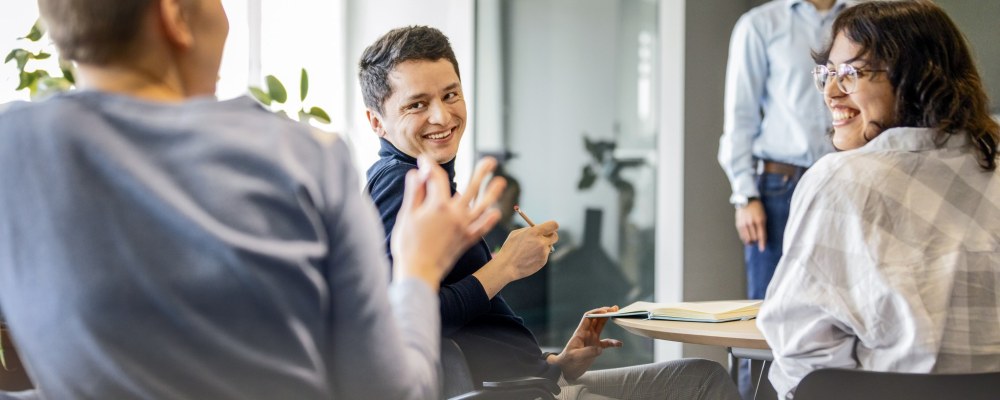 Henkilöitä tapahtumassa, puhuja edessä ja yleisö juttelee toisilleen.