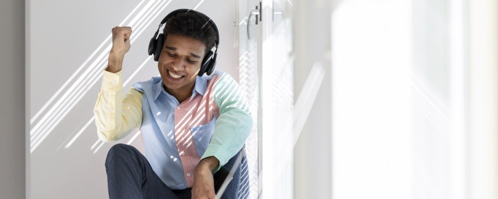 Henkilö istuu ikkunalaudalla kuulokkeet päässään.