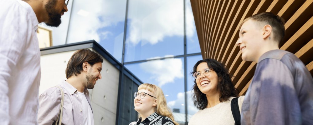 Henkilöitä seisoo ulkona rakennuksen edessä.