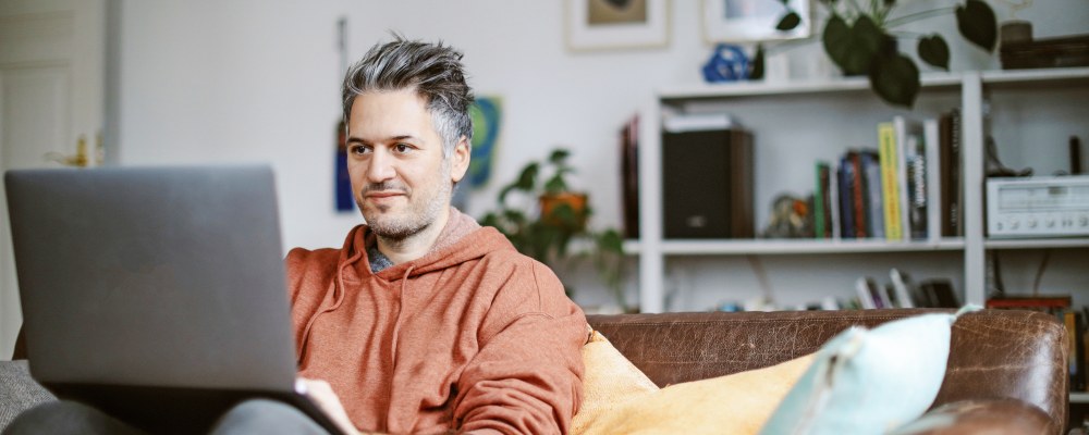 Mies istuu rennosti sohvalla tietokone sylissään