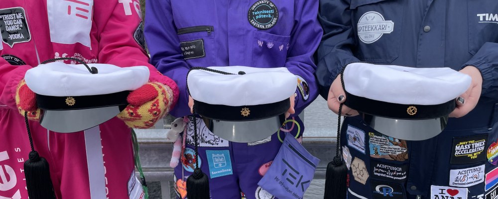 Kolme opiskelijahaalareihin pukeutunutta henkilöä pitelee uutta, itäsuomalaista tupsulakkia.