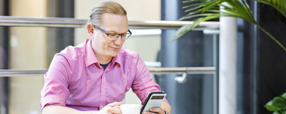 Työntekijä on kahvitauolla ja selaa puhelintaan.