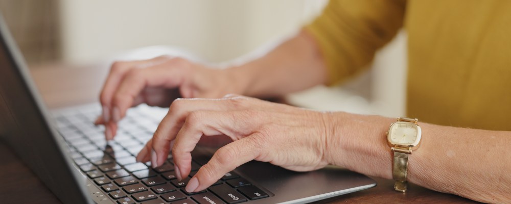 Henkilö keltaisessa paidassa käyttää tietokonetta 