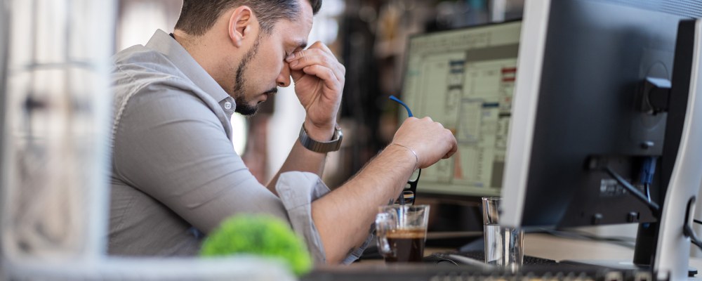 Mies istuu tietokoneen ääressä väsyneen näköisenä.