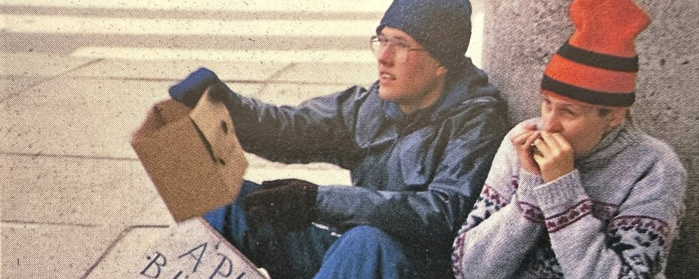 Kaksi nuorta henkilöä istuu maassa keräämässä rahaa.