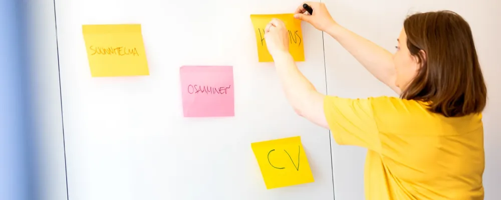 Uravalmentaja laittaa post-it lappuja valkotaululle