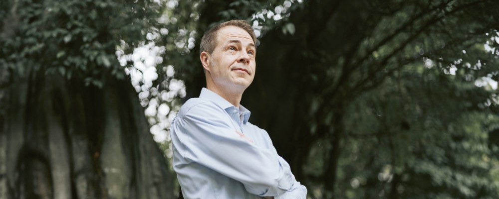 Sami Sivola seisoo isojen puiden edessä kädet puuskassa.