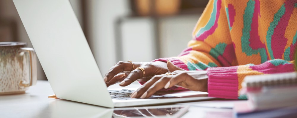 Värikkääseen neuleeseen pukeutunut nuorehko henkilö läppärin ääressä.