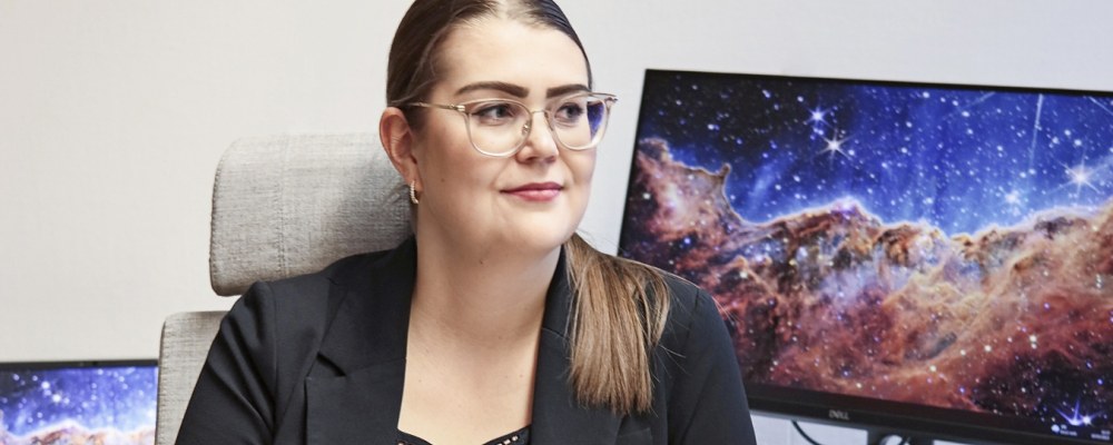 Kiira Tiensuu istuu tietokoneen edessä, tietokoneen näytöllä on avaruusmaisema.