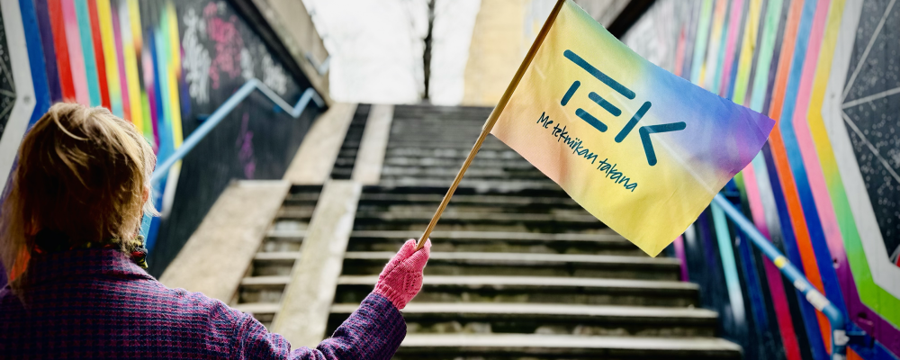 Henkilö heiluttaa TEKin sateenkaarevaa lippua värikkään portaikon alla.