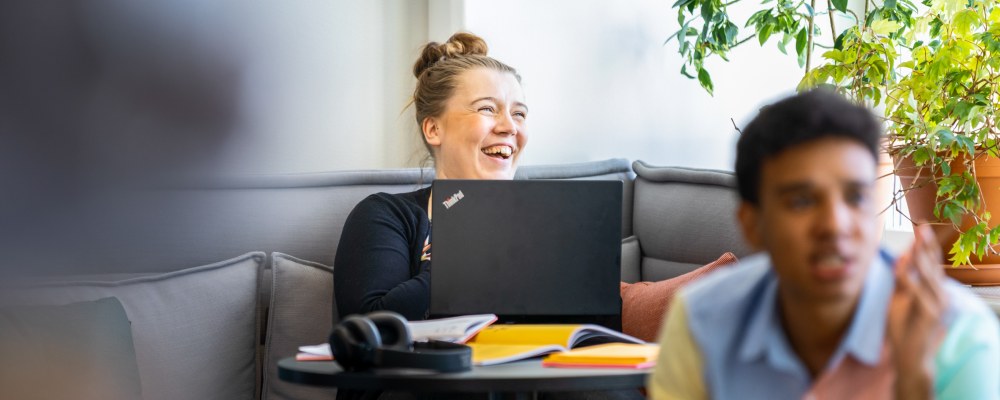 Kaksi henkilöä lounge-tilassa, taaimmainen iloitsee.