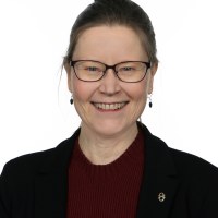 Tuija Kuusistolla on ruskeat hiukset nutturalla, siniset silmät, viininpunainen villapaita ja musta jakku