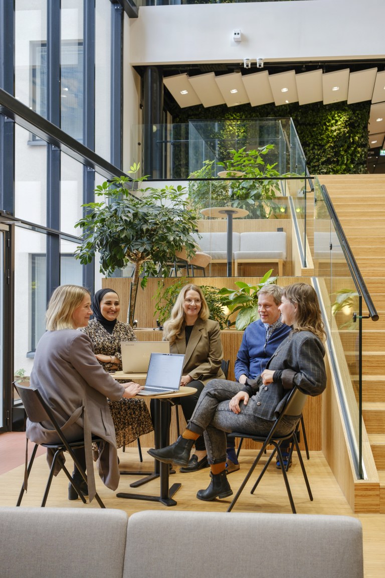 Swecon työntekijöitä istuu ja keskustelee pöytien ääressä.