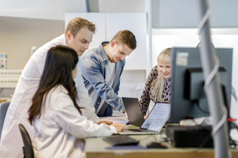 Tiimi on kokoontunut työpöydän äärelle keskustelemaan.