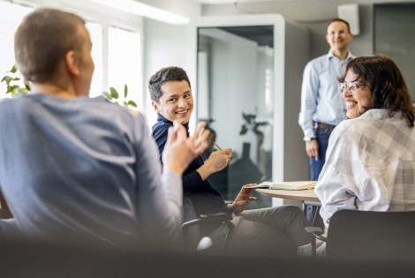 Henkilöitä tapahtumassa, puhuja edessä ja yleisö juttelee toisilleen.