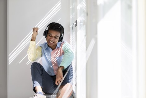 Henkilö istuu ikkunalaudalla kuulokkeet päässään.