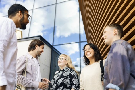 Henkilöitä seisoo ulkona rakennuksen edessä.