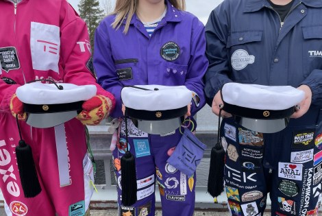 Kolme opiskelijahaalareihin pukeutunutta henkilöä pitelee uutta, itäsuomalaista tupsulakkia.