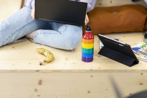 Henkilö istuu portaalla läppäri sylissään, vieressä sateenkaaren värinen juomapullo.