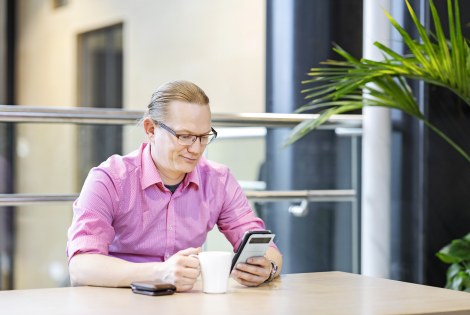 Työntekijä on kahvitauolla ja selaa puhelintaan.