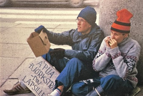 Kaksi nuorta henkilöä istuu maassa keräämässä rahaa.