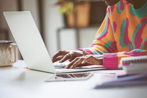 Värikkääseen neuleeseen pukeutunut nuorehko henkilö läppärin ääressä.