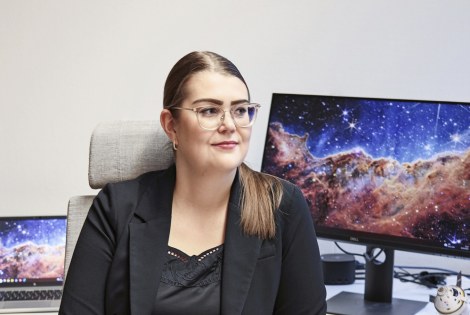 Kiira Tiensuu istuu tietokoneen edessä, tietokoneen näytöllä on avaruusmaisema.