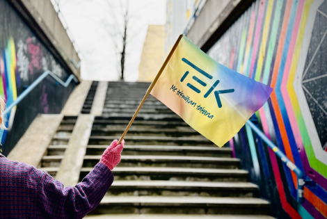 Henkilö heiluttaa TEKin sateenkaarevaa lippua värikkään portaikon alla.