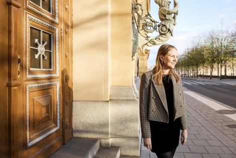 Heta Kosonen seisoo kadulla, ulko-oven edessä.